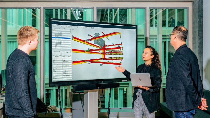 Photograph of a student presenting her work to two others on a large screen.