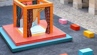 A photograph of an installation depicting a four poster bed in colours of blue, pink and orange, situated in a square of the Hôtel de la Marine.