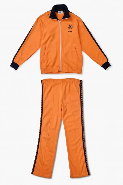 A photograph of an orange and black tracksuit set laid flat against a white background.