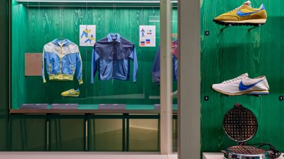 A photograph of an exhibition displaying shoes and apparel against green backdrops.