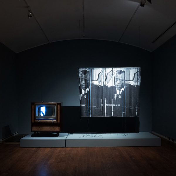 Photograph of an exhibition showing a dark room with art projected on to a screen.