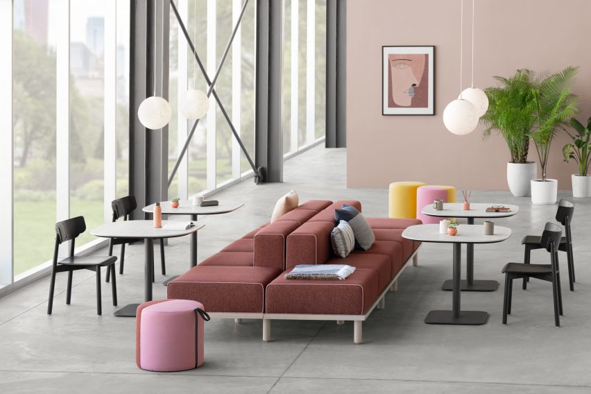 A photograph of two cushioned benches in tones of red and pink, facing back to back. They each have white tables and black chairs either side, with a large window and pink walls surrounding them.