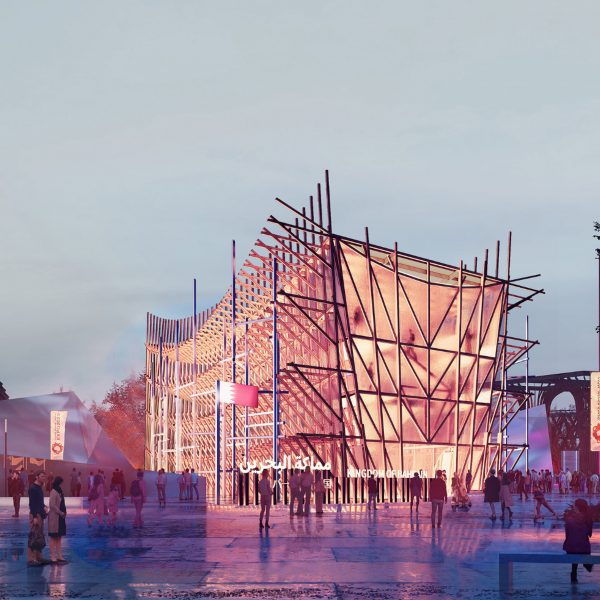 A photograph of an illuminated building in tones of pink, amongst a street with multiple people around it and a grey sky above.