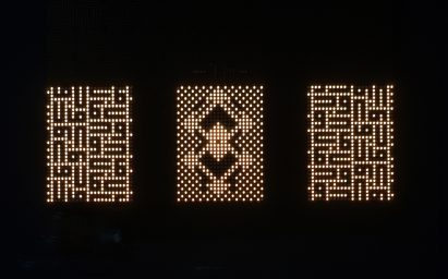A photograph of a lighting installation, which consists of three rectangles with different illuminated patterns inside them, surrounded entirely by black.