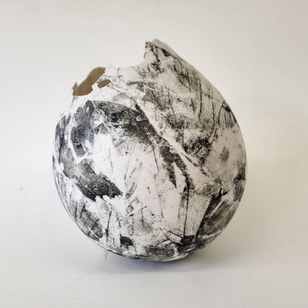 A photograph of a ceramic sphere, in tones of black and white, against a beige backdrop.
