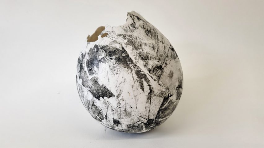 A photograph of a ceramic sphere, in tones of black and white, against a beige backdrop.
