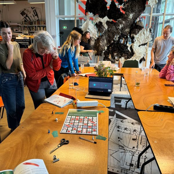 A photograph of people standing around a wooden table, interacting with one another.