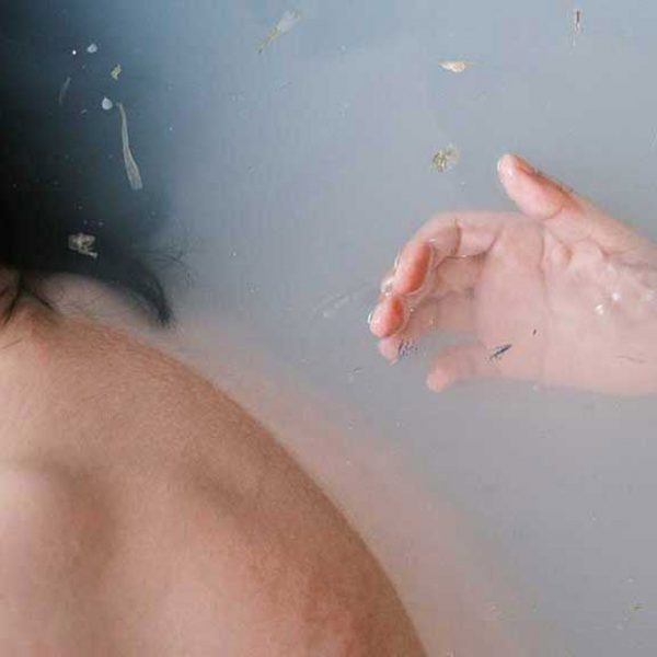 A photograph of a person submerged in water. There is a hand behind them, reaching towards them.