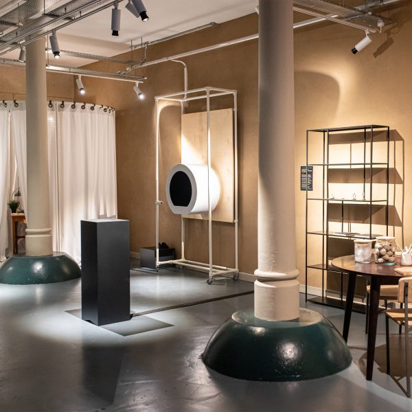 A photograph of a room in tones of grey and brown, with shelving, tables and chairs in the space.