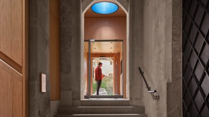 A photograph of the inside of a church in warm tones of beige and brown, with a person in a doorway.