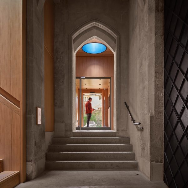 A photograph of the inside of a church in warm tones of beige and brown, with a person in a doorway.