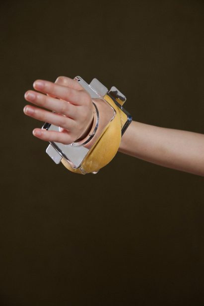 Photo of a person's wrist wearing a chunky bangle made of two pieces of square, flat, shiny silver metal with a bagel-like baked dough form pressed in between
