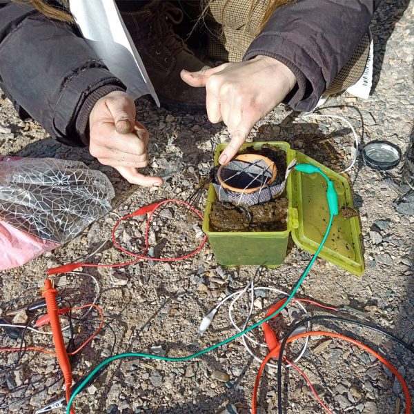 A photograph of a person's hands interacting with a design piece, consisting of a green box connected to various wires.