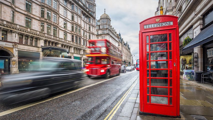 A photograph of a street in London, with a red telephone box on the pavement, cars and a red bus driving past.