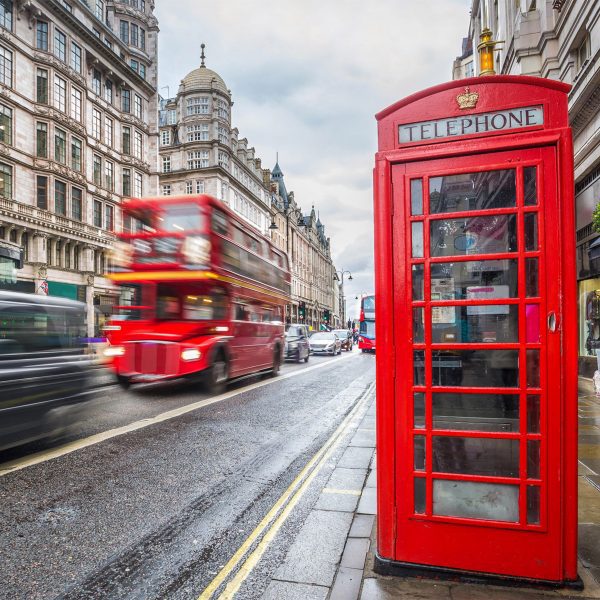 A photograph of a street in London, with a red telephone box on the pavement, cars and a red bus driving past.