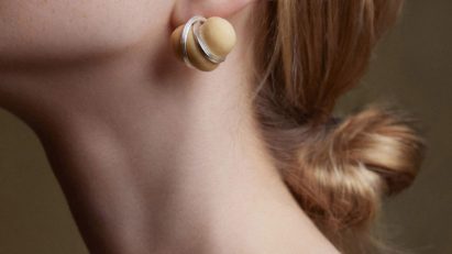 Photo of a woman from the shoulders up wearing earrings made of small baked bread dough wrapped in a metal wire frame from Rising collection by Cindy Xinyi Wu