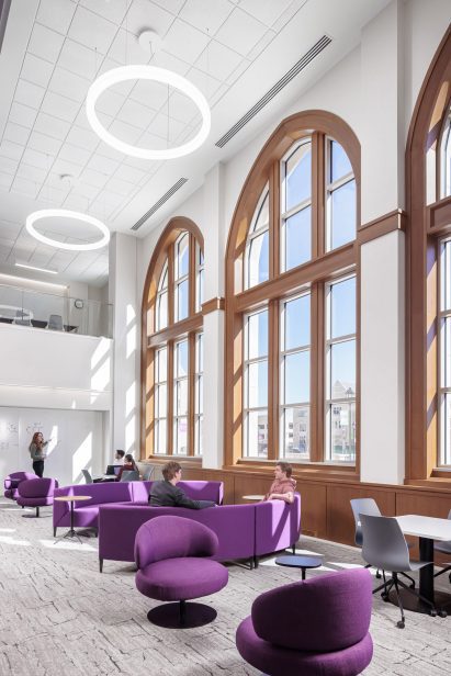 Double-height lounge space with purple furniture and pointed-arch windows