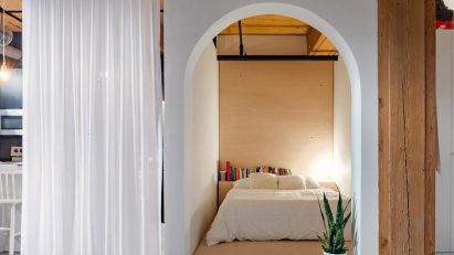 A photograph of a compartment within a large room; it has an arched entrance and inside is a bed.
