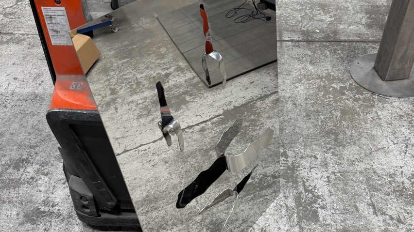 A photograph of a mirror stood on a grey concrete floor. It has details of rips and tears on it.