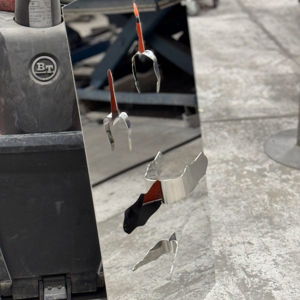 A photograph of a mirror stood on a grey concrete floor. It has details of rips and tears on it.