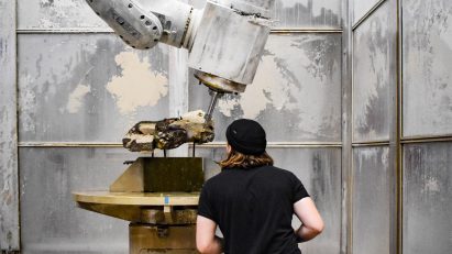 A photograph of a student using a large machine to create an object in tones of white and brown.