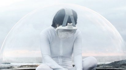 A photograph of a person in white clothing, with a VR headset on, sat on the ground in tones of brown. There is a translucent semi-sphere framing them against a pale blue backdrop.
