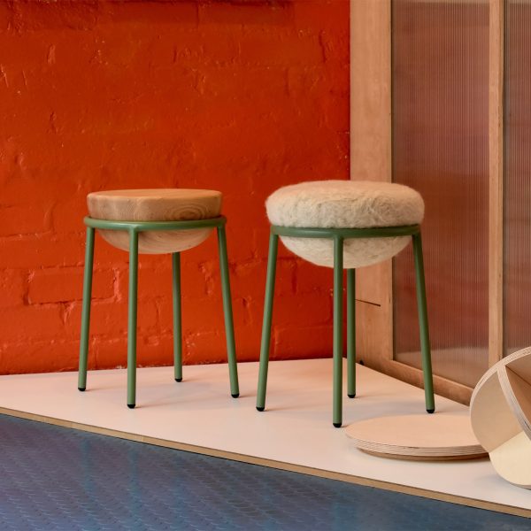 A photograph of two stools, with beige circular seats and green legs. They are against a red backdrop.