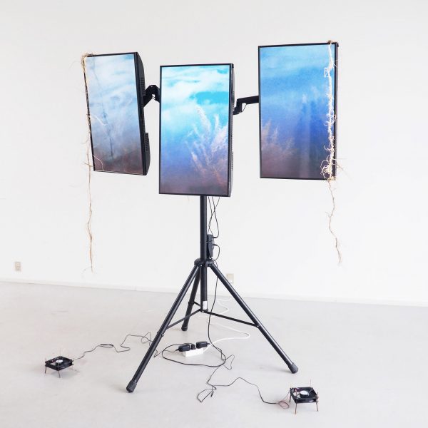 A photograph of an installation, a structure with black legs, holding up three blue rectangular screens.