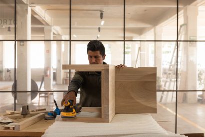 Worker working on wooden chair in light filled workshop