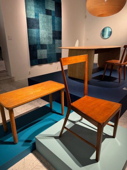 Chairs and tables displayed on exhibition plinths with rug on wall
