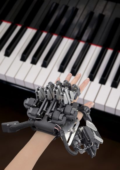 Photo of a hand hovering over piano keys while wearing a complex exoskeleton