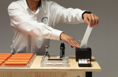 A photograph of a person wearing a white shirt, interacting with a design installation, which is situated atop a desk.