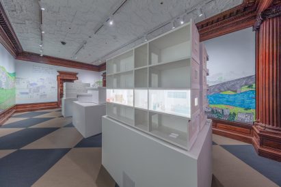 Photo of a cross-section architectural model of an apartment buiding with one apartment lit up and decorated with illustrations