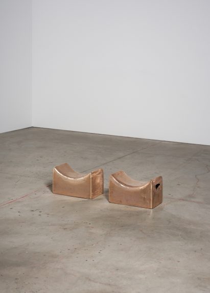 Photo of two copper headrests sitting lined up on a concrete gallery floor
