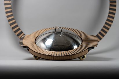 Photo of a circular cardboard object with a metal lid and skateboard wheels created by students Emily Straughn, Paul Goss and Kelly Chen