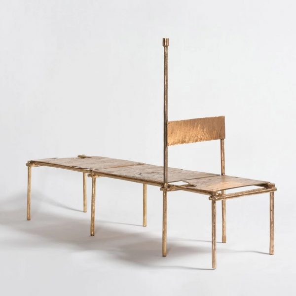 Studio photo of a daybed made from cast copper. At one end a backrest forms a chair, while a linear element extending vertically from the frame adds a candlestick from Oriki act II by Nifemi Marcus-Bello