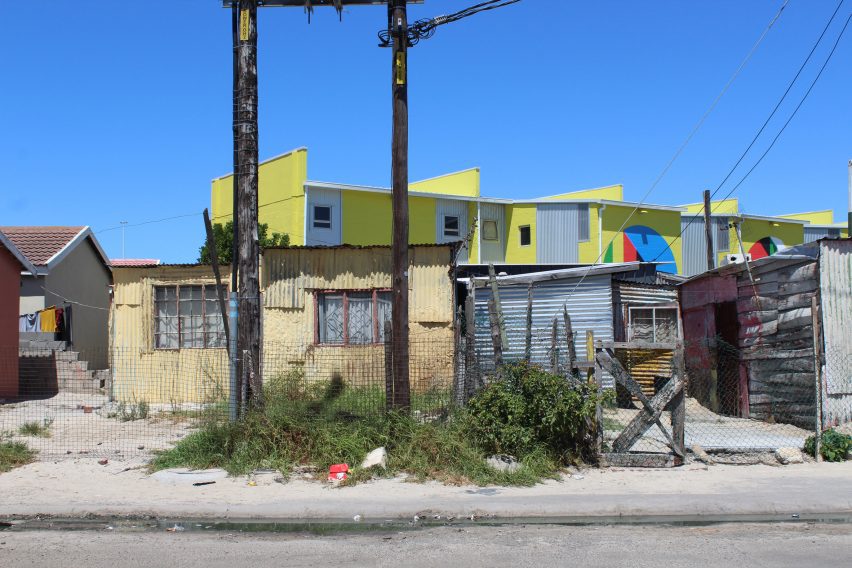 Photo of the rooftops and bright yellow second storeys of the BT-Soweto development sticking out over a row of shacks in a neighbouring street