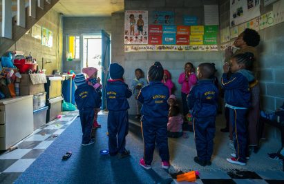 Photo of children playing within a creche made of concrete block walls covered with bright posters and artworks