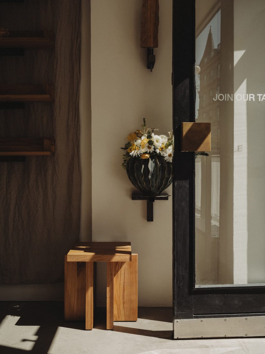 Photograph of the entrance to the minimalist interior, showing a glass door and a geometric, oakwood stool.
