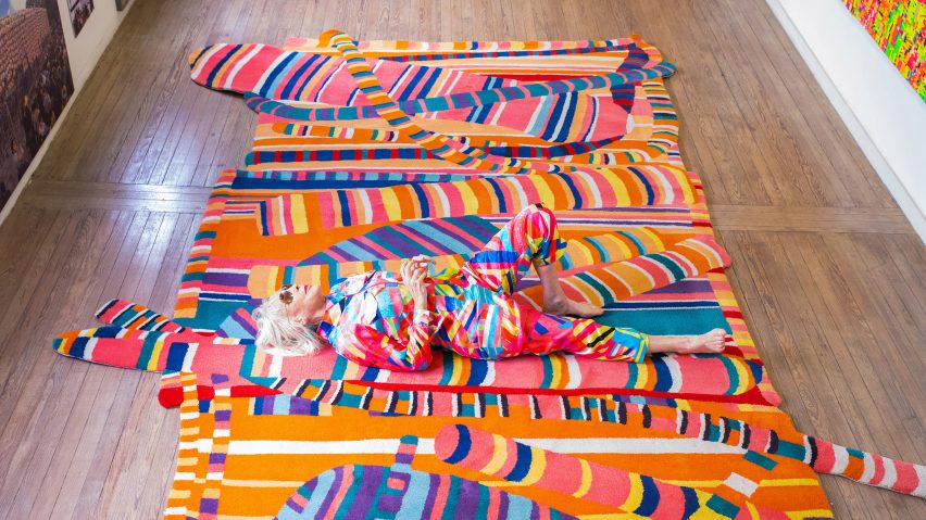 Photo of Marta Minujín lying on a colourful, pattern rug