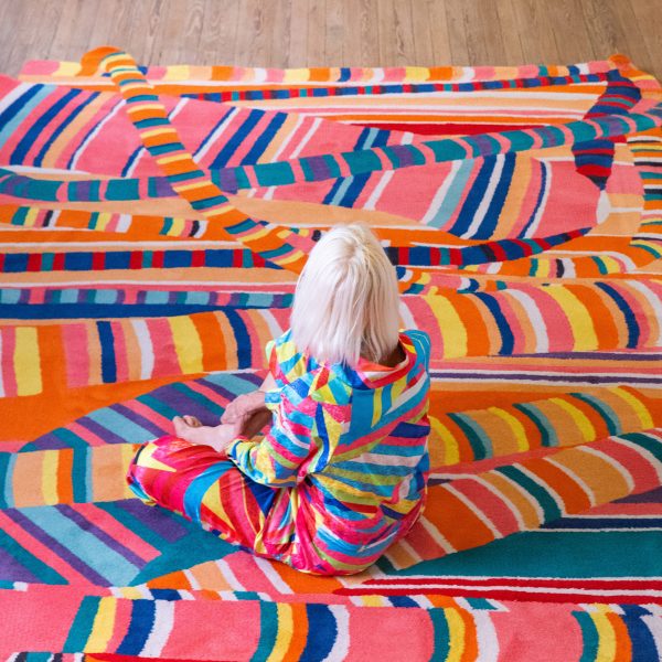 Photo of Marta Minujín sitting on a colourful, pattern rug