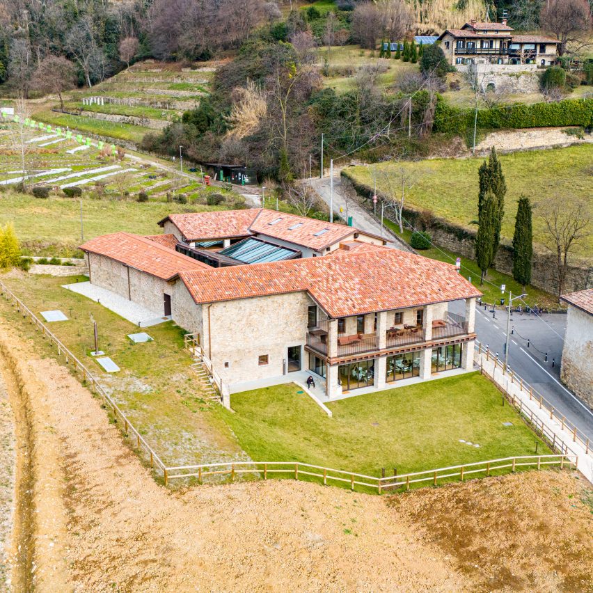 a photograph of a stone building in tones of beige with a red brick roof, within a large green field