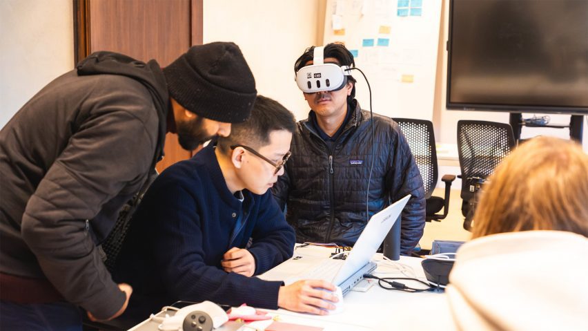 A photograph of students on an interaction design course. One is wearing a VR headset and the others are working at a laptop.