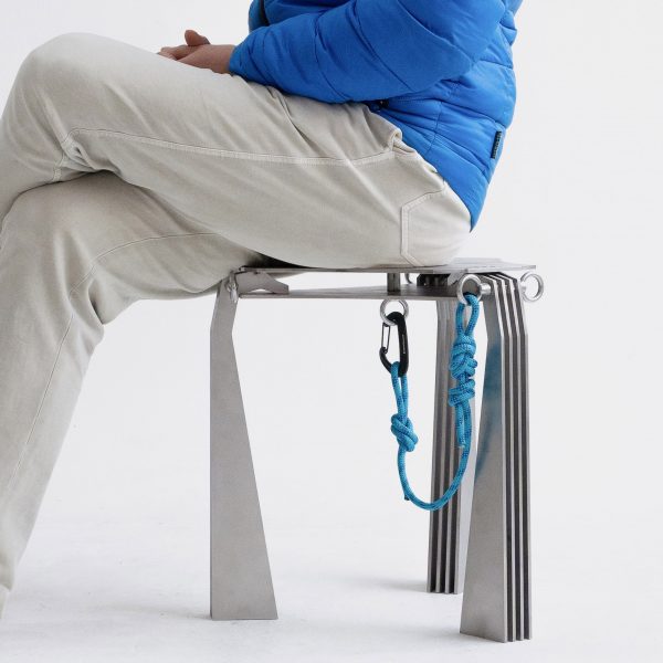 A photograph of a person sat on a silver stool