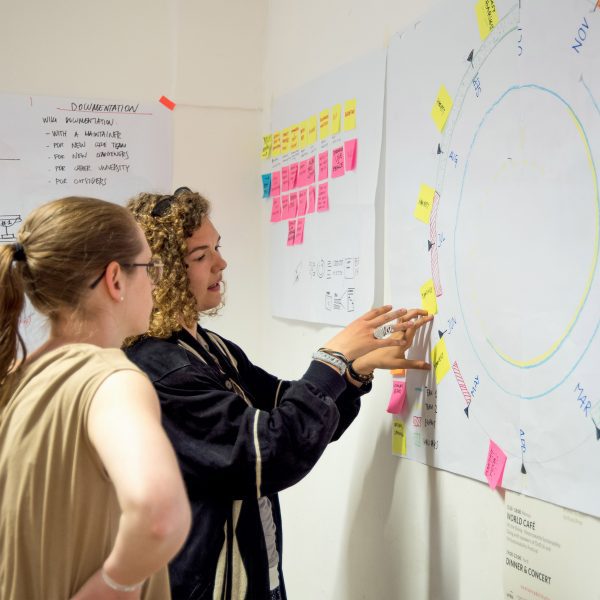 A photograph of two people referencing a poster on a wall.
