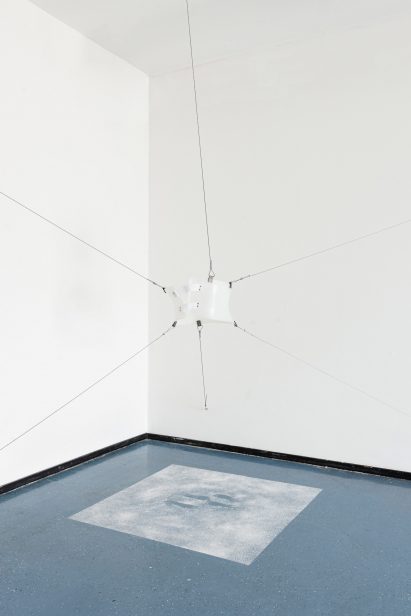 A photograph of a hanging white installation, in a room with white walls and a blue floor.