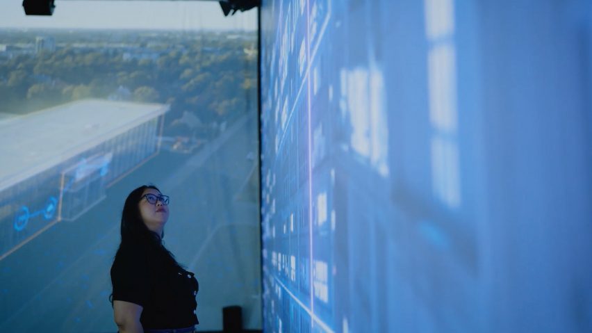 a person standing in front of screens with blue projections on them