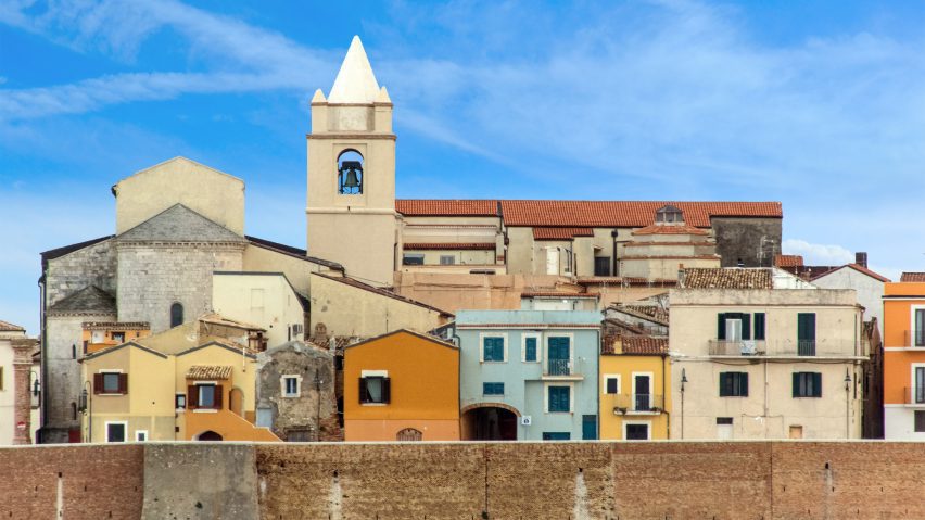 A photograph of stone buildings in tones of blue, orange and pink against a blue sky