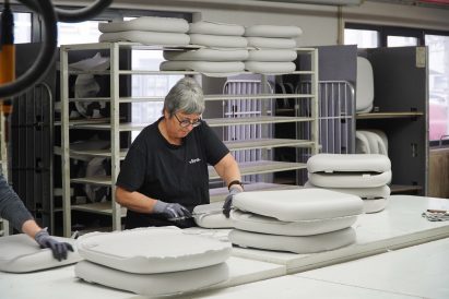 Photo of a woman cutting the excess edge material off from moulded foam seating pads in a factory