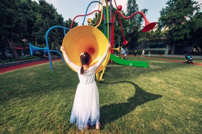 Girl holding the edges of a yellow speaking tube in a park